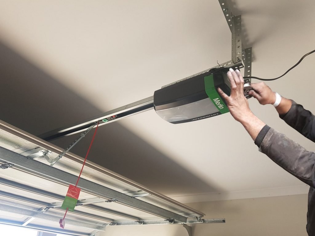 Technician installing a Merlin garage door opener in a residential garage